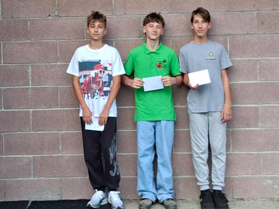 I tre ragazzi del podio U15 in appoggio, con la busta del premio in mano, davanti al muro del poligono